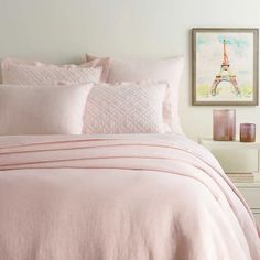 a bed with pink comforter and pillows in a white room next to a painting on the wall