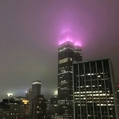 the city skyline is lit up with purple lights in the foggy night time sky