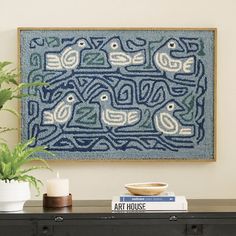 a blue and white painting on the wall above a black table with books, plant and vase