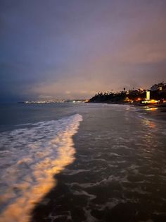 an ocean beach with waves coming in to the shore and buildings lit up at night