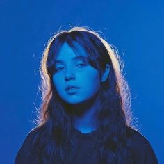 a woman with long hair standing in front of a blue background wearing a black shirt