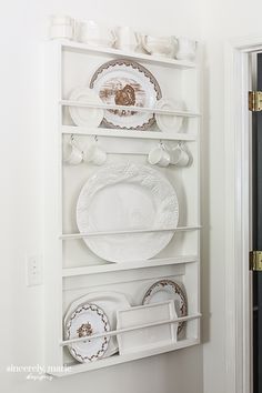 a white shelf filled with plates and dishes on top of it's sides in front of a doorway