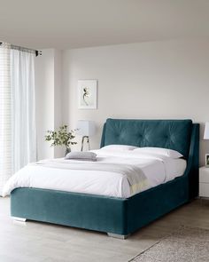 a bed with a blue headboard and foot board in a white room next to a window