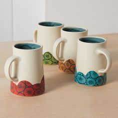 four coffee mugs sitting on top of a wooden table next to eachother