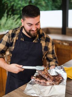 a man in an apron holding a spatula over some meat on top of tin foil