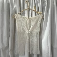 a white sweater hanging on a clothes hanger in front of drapes with curtains behind it