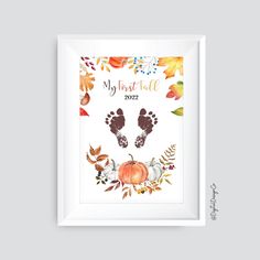 a white frame with an orange and yellow fall print on it, featuring the baby's foot prints