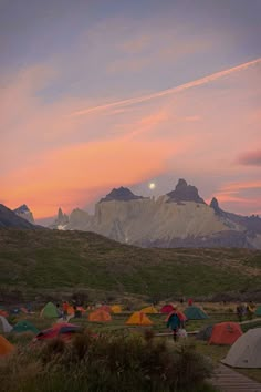 a group of tents set up in the grass with mountains in the background at sunset