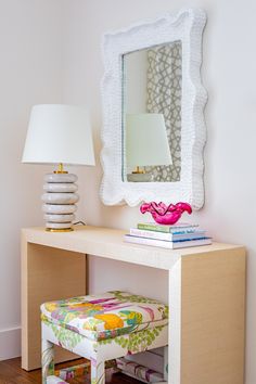 a white table topped with a mirror next to a pink chair and lamp on top of a hard wood floor