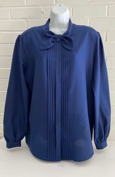 This blouse is a old style classic-unique for sure. Solid navy blue. Hidden buttons down front. Beautiful pleats down front. High neck with simple bow. Loop in the middle of bow with button (so cool). Thin shoulder pads. Please see all pictures for a better detailed description.  Length: 26 1/2" Pit to pit: 23" Sleeve length: 24 1/4"- 24 1/2" Shoulder seam: 6" 100% polyester Attached tag indicates (tall) Professional Blouse, Professional Blouses, Blue Shirt Women, Simple Bow, High Neck Long Sleeve, Business Meeting, Work Attire, Style Classic, Blue Shirt