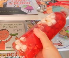 a person holding up a plastic container filled with candy and marshmallows in front of children's books