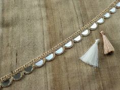 a gold chain with tassels and white stones on it, next to a beige tassel