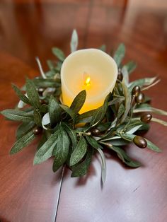 a lit candle sitting on top of a wooden table next to green leaves and berries