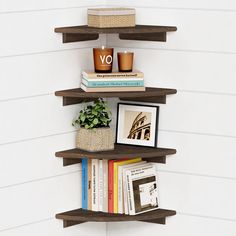 three wooden shelves with books and pictures on them against a white wall in the corner