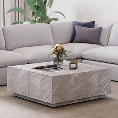 a marble coffee table with flowers on it in front of a couch and large potted plant