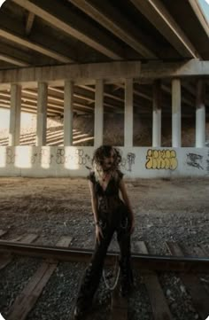 a woman standing on train tracks under a bridge