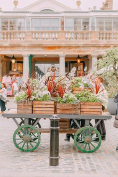 two wooden crates filled with plants sitting on top of a metal table in front of a building