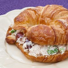 a croissant sandwich with meat and cheese on it sitting on a white plate