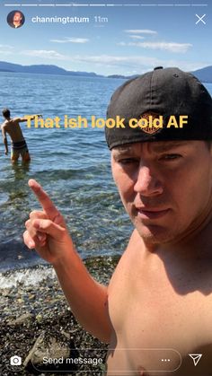 a man with no shirt on standing next to the ocean and pointing his finger up