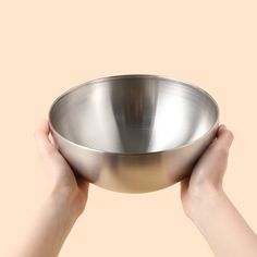 two hands holding a metal bowl in front of a beige background with the bottom half off