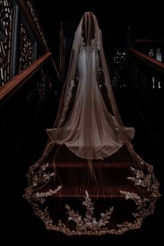 the bride is walking down the stairs in her wedding dress and veil with flowers on it