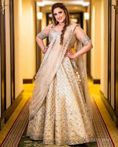 a woman in a white and gold lehenga standing on a hallway with her hands on her hips