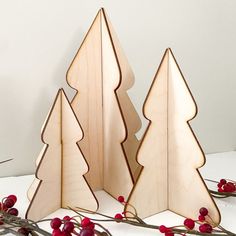 three wooden christmas trees sitting next to each other on a white table with red berries