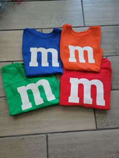 three t - shirts with m and m on them sitting on top of a wooden floor