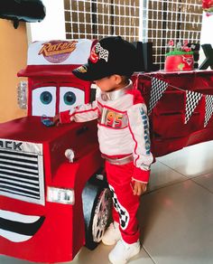 a little boy dressed up as a race car and standing next to a toy truck