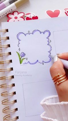 a person is drawing on a page in a notebook with colored pencils next to it