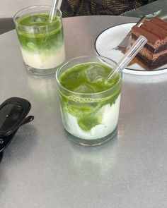 two glasses filled with green liquid sitting on top of a table next to a cell phone