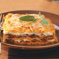 a plate topped with lasagna covered in cheese and sage leaf garnish