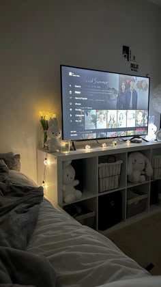 a flat screen tv sitting on top of a white shelf next to a bed in a room