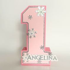 a pink and silver number one with snowflakes on the top, sitting in front of a white background