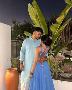 a man and woman standing next to each other in front of a potted plant