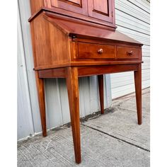 a wooden desk sitting on top of a sidewalk next to a white wall and door