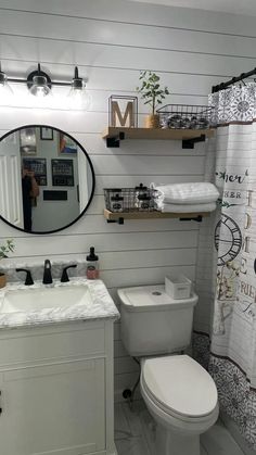 a white toilet sitting next to a sink in a bathroom under a large round mirror