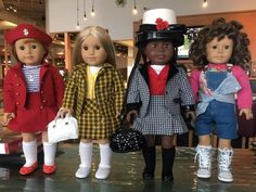 four dolls are standing next to each other in front of a store display case with clothes and hats on