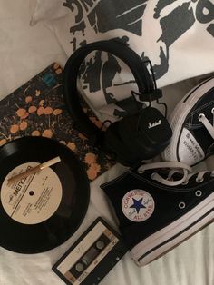 an old record, black and white converse sneakers, and other items are laying on a bed