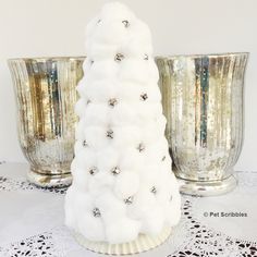 a white christmas tree sitting on top of a table next to two silver vases