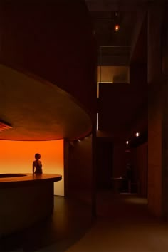 a woman sitting on a bench in front of an orange light at the end of a hallway