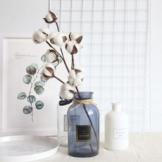 a glass jar with cotton flowers in it next to a white plate and framed photograph