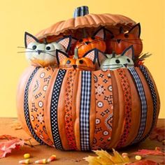 two cats sitting in a pumpkin shaped basket on top of a wooden table with autumn leaves