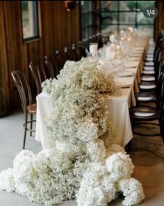 an arrangement of white flowers on a table in a room with long tables and chairs