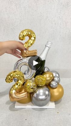 someone is holding a bottle of champagne in front of some balloons that spell out the number two