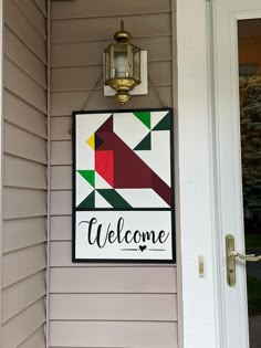 a welcome sign hanging on the side of a house with a light fixture above it