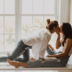 two women are sitting on the windowsill and one is kissing the other's cheek