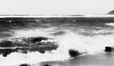 black and white photograph of waves crashing on the beach with an island in the distance