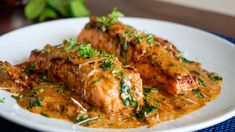 a white plate topped with meat covered in sauce and garnished with parsley