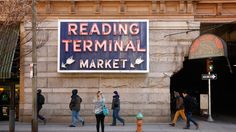 people walking on the sidewalk in front of a building with a sign reading reading terminal market